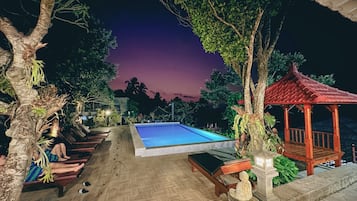 Relax by the serene pool surrounded by lush greenery and a shaded gazebo.