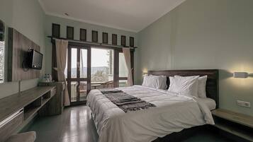 A bedroom with a bed, a desk, a television, and a view of the outdoors.