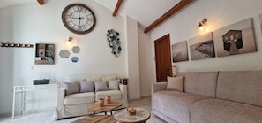 Uma sala de estar com sofá, mesa de centro, relógio e quadros nas paredes.