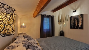 A bedroom with a bed, a decorative wall panel, a mirror, and a vase with plants.