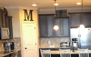 Una cocina moderna con armarios oscuros, una puerta blanca, microondas, tostadora, refrigerador e iluminación colgante.