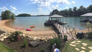 A lakeside deck with kayaks, a covered seating area, and a dock extending into the water. - Lakefront home with private beach  & unbelievable sunsets on Lake Keowee (Seneca)