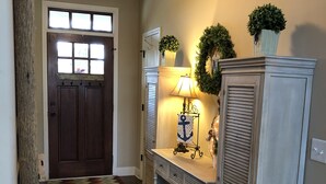A hallway with a wooden floor, a door with a window, a console table with a lamp, and a cabinet. - Lakefront home with private beach  & unbelievable sunsets on Lake Keowee (Seneca)