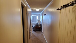 A narrow hallway with carpeted floors, a door on the left, and a lamp on the right.