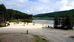A beach with a playground, a small building, and a lake.