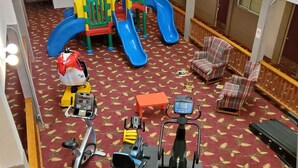 A children's play area with slides and climbing structures, a small table, and exercise equipment on a patterned carpet.