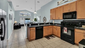 A modern kitchen with wooden cabinets, a black stove, and a large island. - Disney home- Private Pool&Hot Tub! 4b/3ba, 7 beds!! Close to all the  parks!!! (Kissimmee)