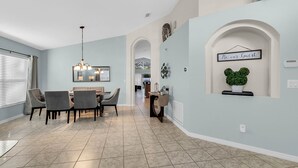 A dining area with a table and chairs, a chandelier, and a sign that reads "Be our guest." - Disney home- Private Pool&Hot Tub! 4b/3ba, 7 beds!! Close to all the  parks!!! (Kissimmee)