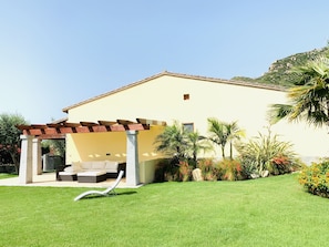 A house with a covered patio, a lawn, and a mountain in the background.