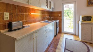 Una cocina con tostadora integrada, un lavamanos y un microondas. Se ve follaje verde a través de la ventana.