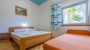 A bedroom with a wooden bed, a nightstand, a window with curtains, and a painting on the wall. - Holiday apartment mit Terrasse und Klimaanlage (Dramalj)