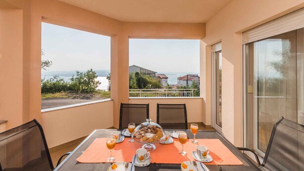 A balcony with a table set for breakfast, overlooking a scenic view of the sea and buildings.