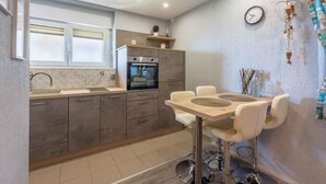 A modern kitchen with grey cabinets, a built-in oven, a sink, and a dining area with a round table and chairs.