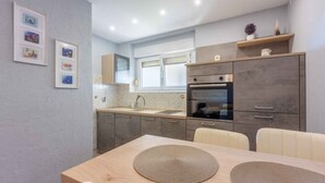 A modern kitchen with a dining area, featuring a large table with placemats, a built-in oven, and a window above the sink.