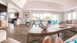 A spacious living room with a dining area, large windows, and a view of the outdoors. - Pool, Hot Tub, 50 steps to sand, Pool table (St. Augustine)