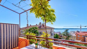 A balcony with a table set for two, overlooking a coastal cityscape with buildings and a crane in the distance. - Holiday apartment with balcony and air conditioning (Crikvenica)