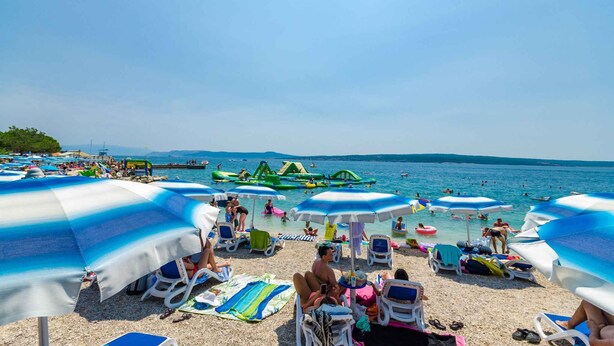 A beach with umbrellas, lounge chairs, and people swimming and sunbathing. - Holiday apartment with balcony and air conditioning (Crikvenica)