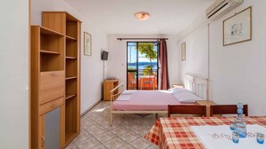 A bedroom with a bed, a table with drinks, a wardrobe, and a view of the sea through a window. - Holiday apartment with balcony and air conditioning (Crikvenica)