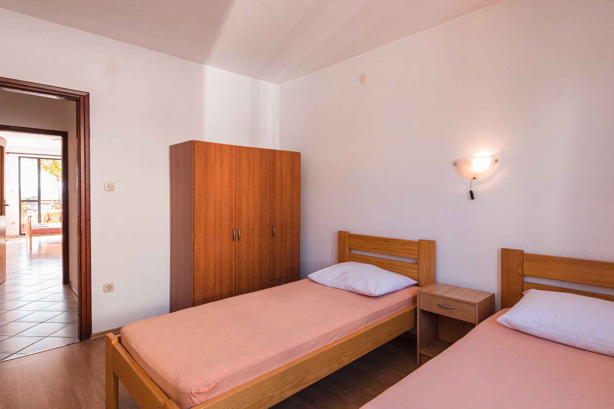 Une petite chambre propre, avec deux lits simples, une armoire en bois et une table de chevet.