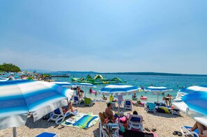 En strand med parasoller, solstolar och folk som badar och solar.
