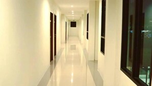 A long, well-lit corridor with white walls and a shiny floor, leading to a darkened room at the end. - The Hub Suratthani Hotel (Surat Thani)