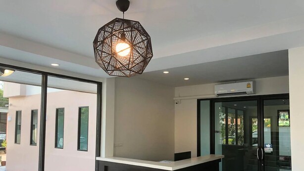 A modern reception area with a black and white counter, a geometric pendant light, and a glass door leading outside. - The Hub Suratthani Hotel (Surat Thani)
