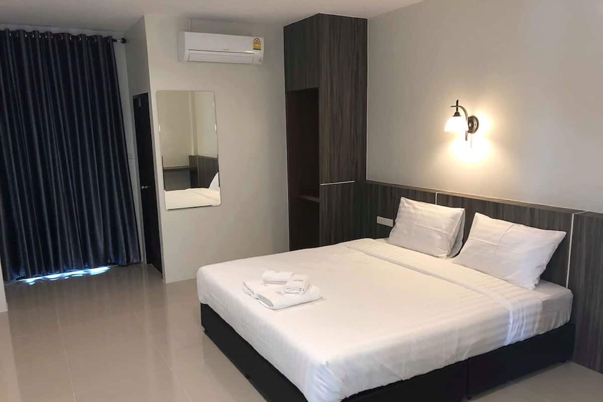 A modern hotel room with a large bed, a mirror, an air conditioning unit, and a wall-mounted light fixture.