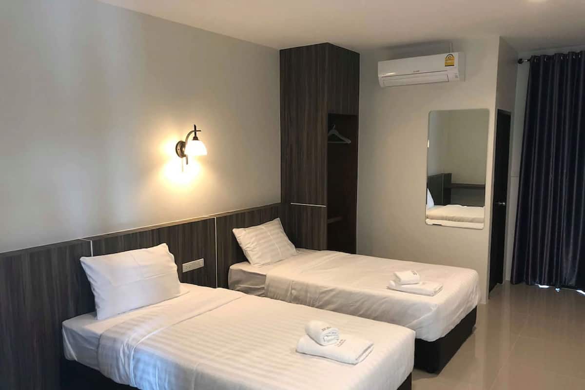 A hotel room with two single beds, a wall-mounted air conditioner, a mirror, and a dark curtain.