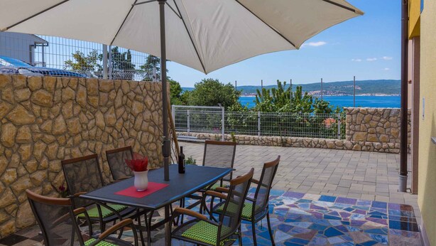 Eine Terrasse im Freien mit Tisch, Stühlen und einem großen Sonnenschirm, begleitet von einer Steinmauer.