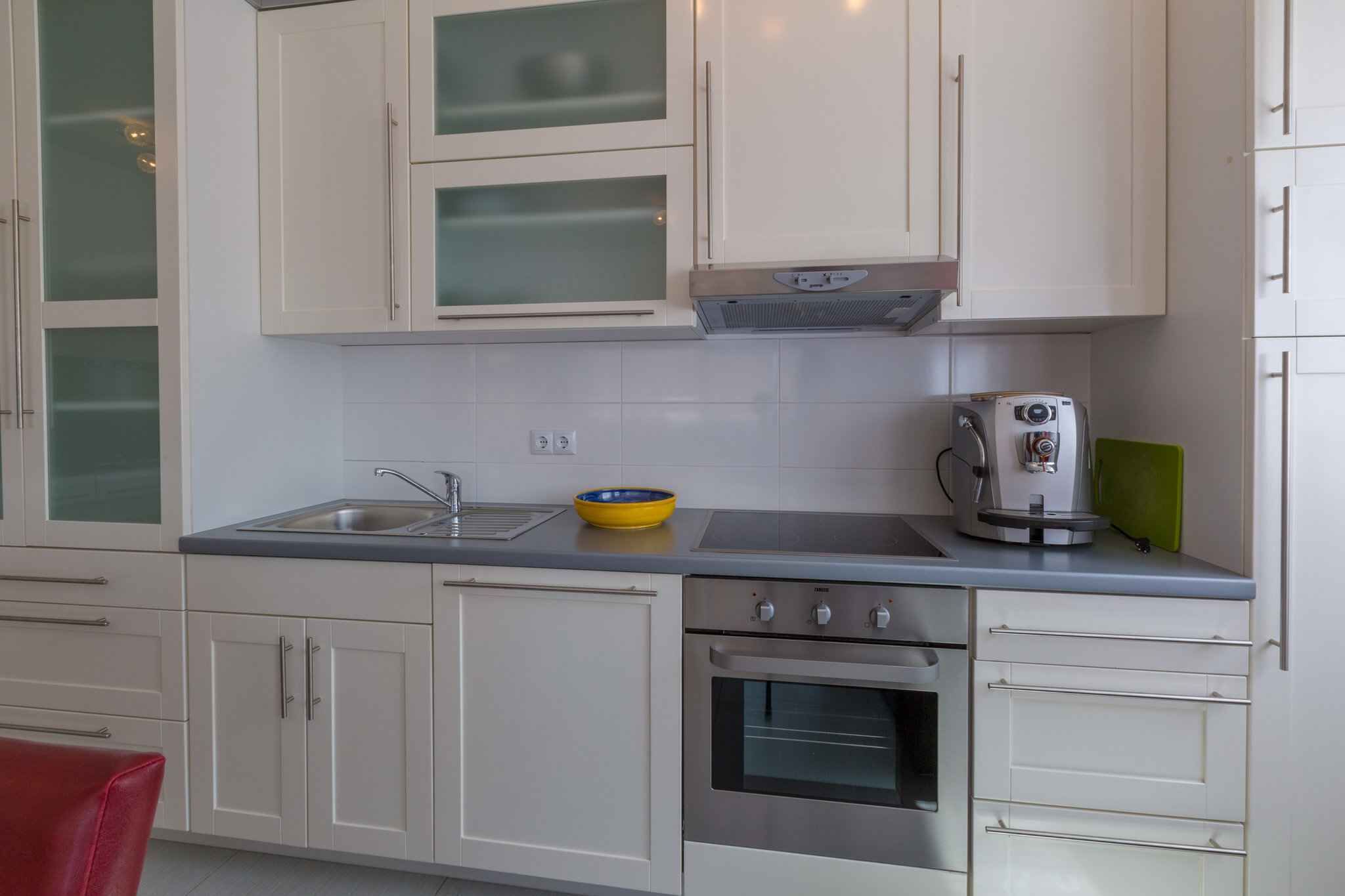 A kitchen with white cabinets, a stainless steel sink, a built-in oven, and a coffee maker.