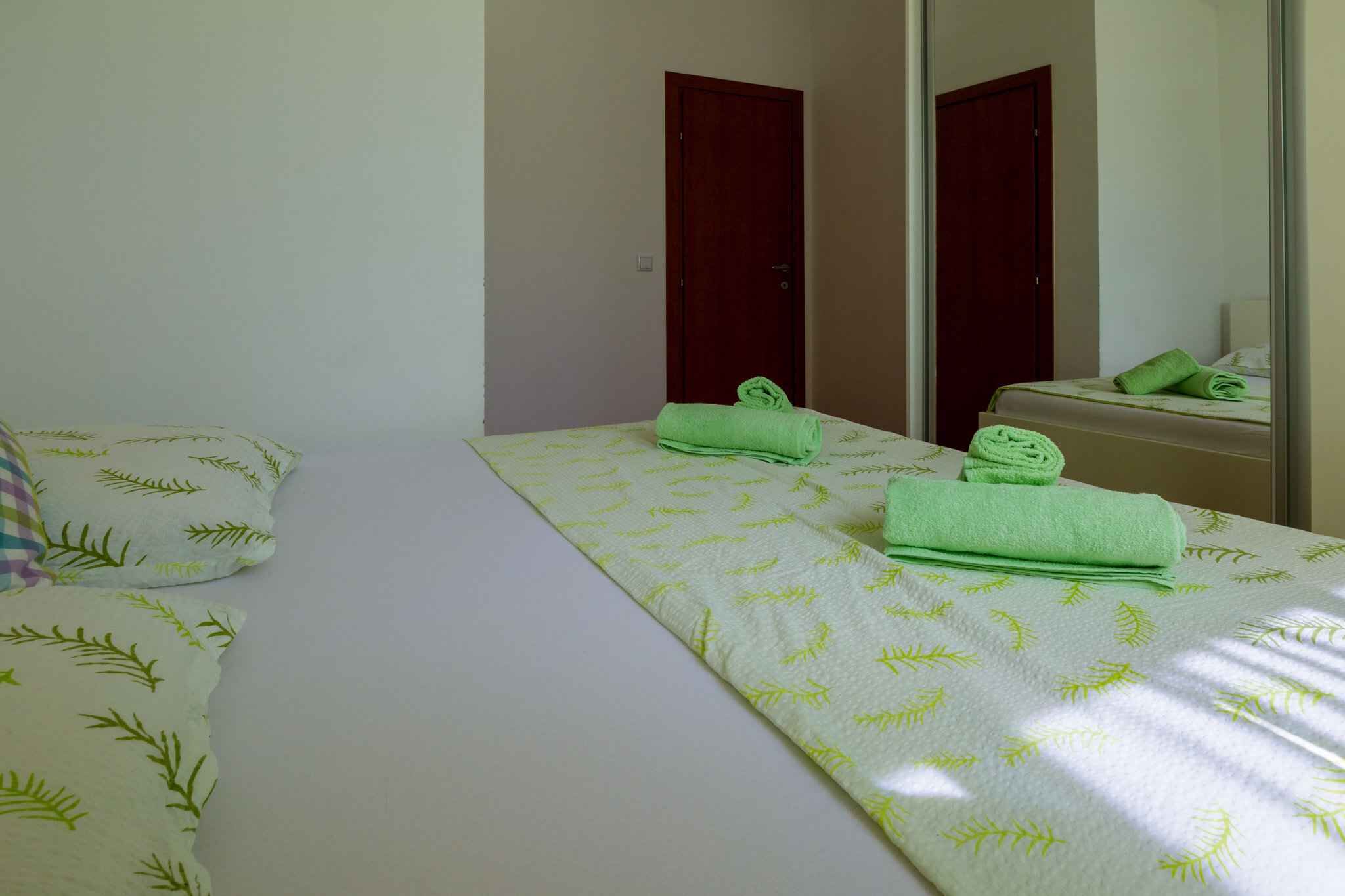 A hotel room with a bed, two doors, and a mirror reflecting the bed and a green towel.