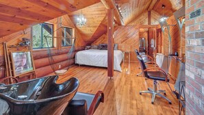 Une cabane chaleureuse avec un intérieur en bois, un lit, un coin repas avec des chaises et une grande fenêtre.