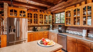 Une cuisine rustique aménagée dans une cabane en bois, avec un réfrigérateur en acier inoxydable, des armoires en bois et un plan de travail en granit.