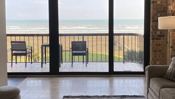 A balcony with a view of the ocean, furnished with two chairs and a small table.