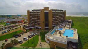 A large hotel with a central courtyard, a swimming pool, and a view of the ocean.
