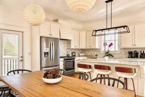 A modern kitchen with white cabinetry, stainless steel appliances, and a wooden dining table with chairs.