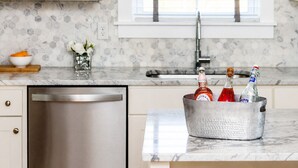 Una cocina con encimera de mármol, lavavajillas de acero inoxidable y un cubo de metal con botellas.