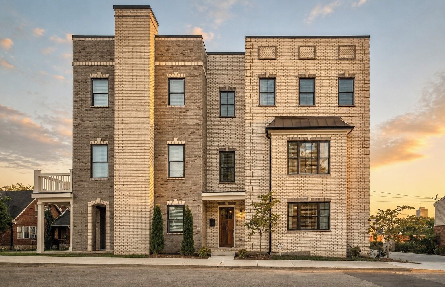 A multi-story brick building with a central entrance, windows on each floor, and a small porch area.