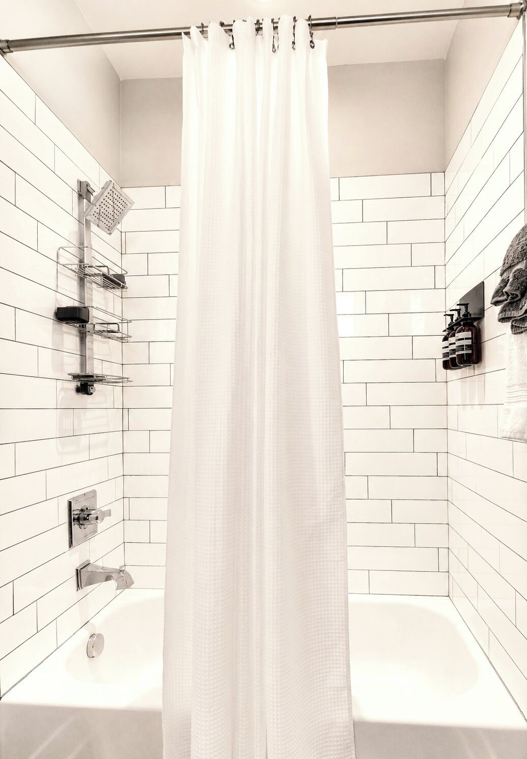 A modern bathroom with white tiled walls, a shower with a curtain, and a bathtub.