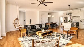Una sala de estar moderna con sofá, mesa de centro y sillas, un comedor con mesa y sillas, una cocina con electrodomésticos y un ventilador de techo.