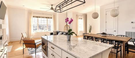 Una cocina moderna con una isla central, una mesa de comedor de madera e iluminación colgante.