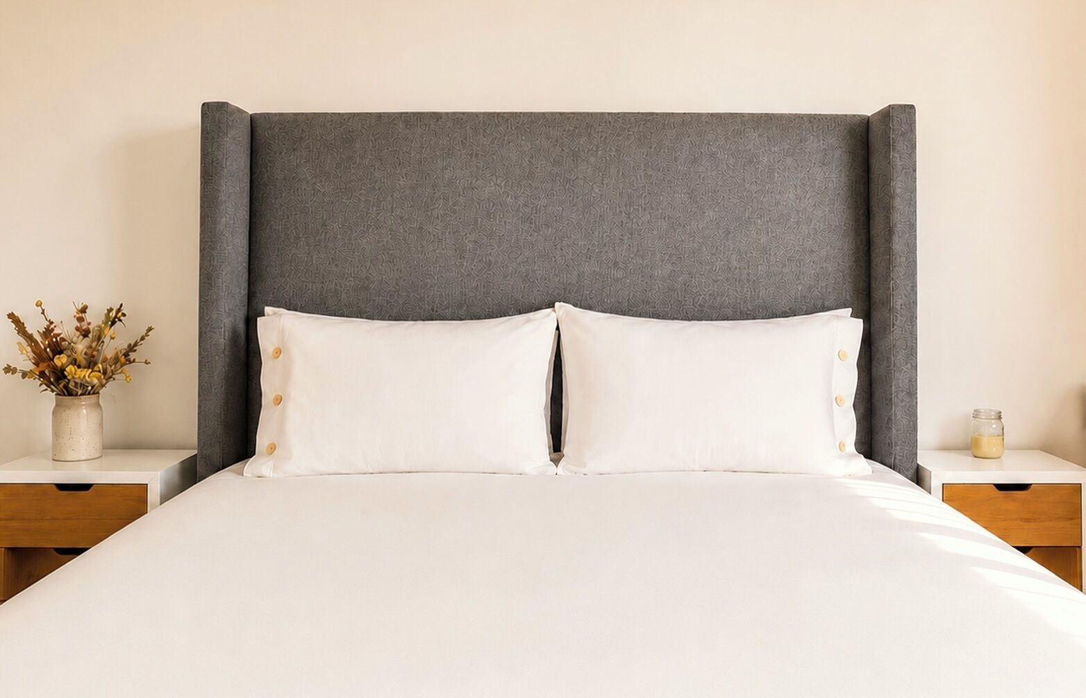 A bed with a grey headboard, two white pillows, and a white bedspread.