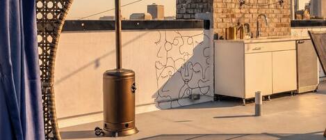 A rooftop terrace with a bed, a water dispenser, and a view of the cityscape.