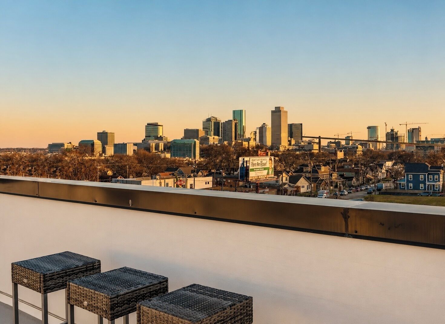 Ein Stadtbild bei Sonnenuntergang mit modernen Gebäuden, einer Werbetafel und einer Reihe von Korbstühlen auf einem Balkon.