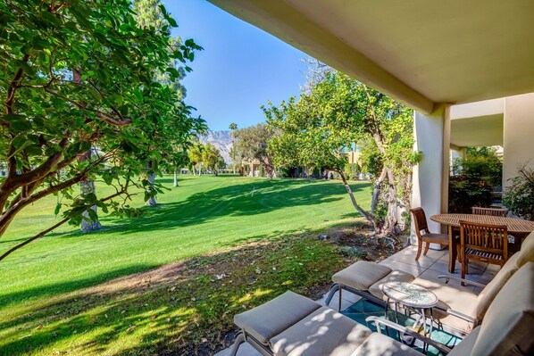 A patio with outdoor seating, a pool, and a view of a well-maintained lawn and trees.