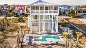 A two-story beachfront house with a pool, surrounded by a sandy beach and palm trees. - Paradise Point: Luxury Beachfront Home with Views (Pawleys Island)