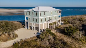 A two-story beachfront house with a balcony, a sandy driveway, and a view of the ocean. - Paradise Point: Luxury Beachfront Home with Views (Pawleys Island)