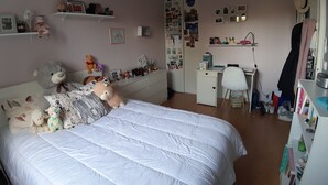 Een slaapkamer met een bed, een bureau en planken met verschillende spullen.
