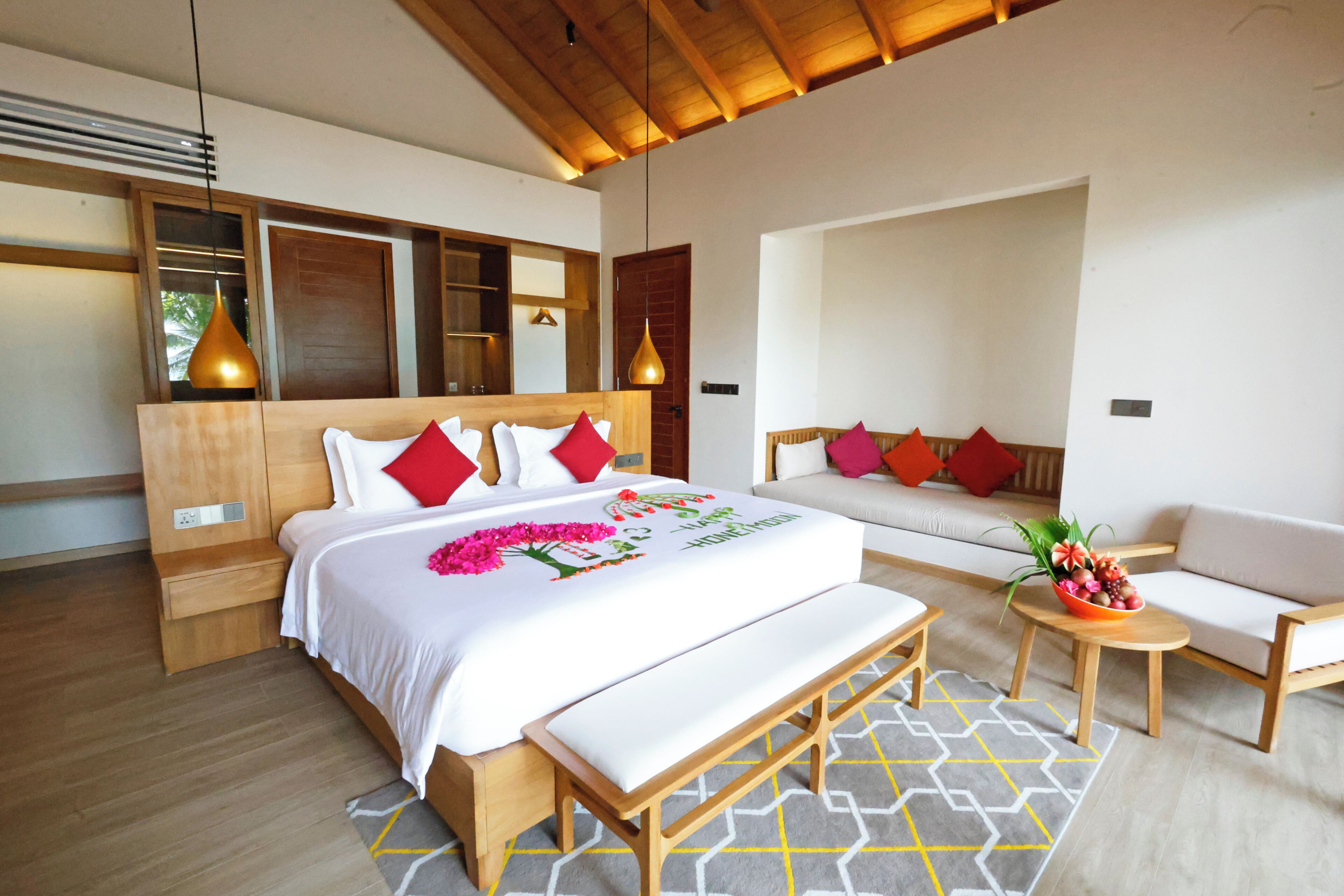 A modern hotel room with a large bed, a bench, a sofa, and a small table with a flower arrangement.