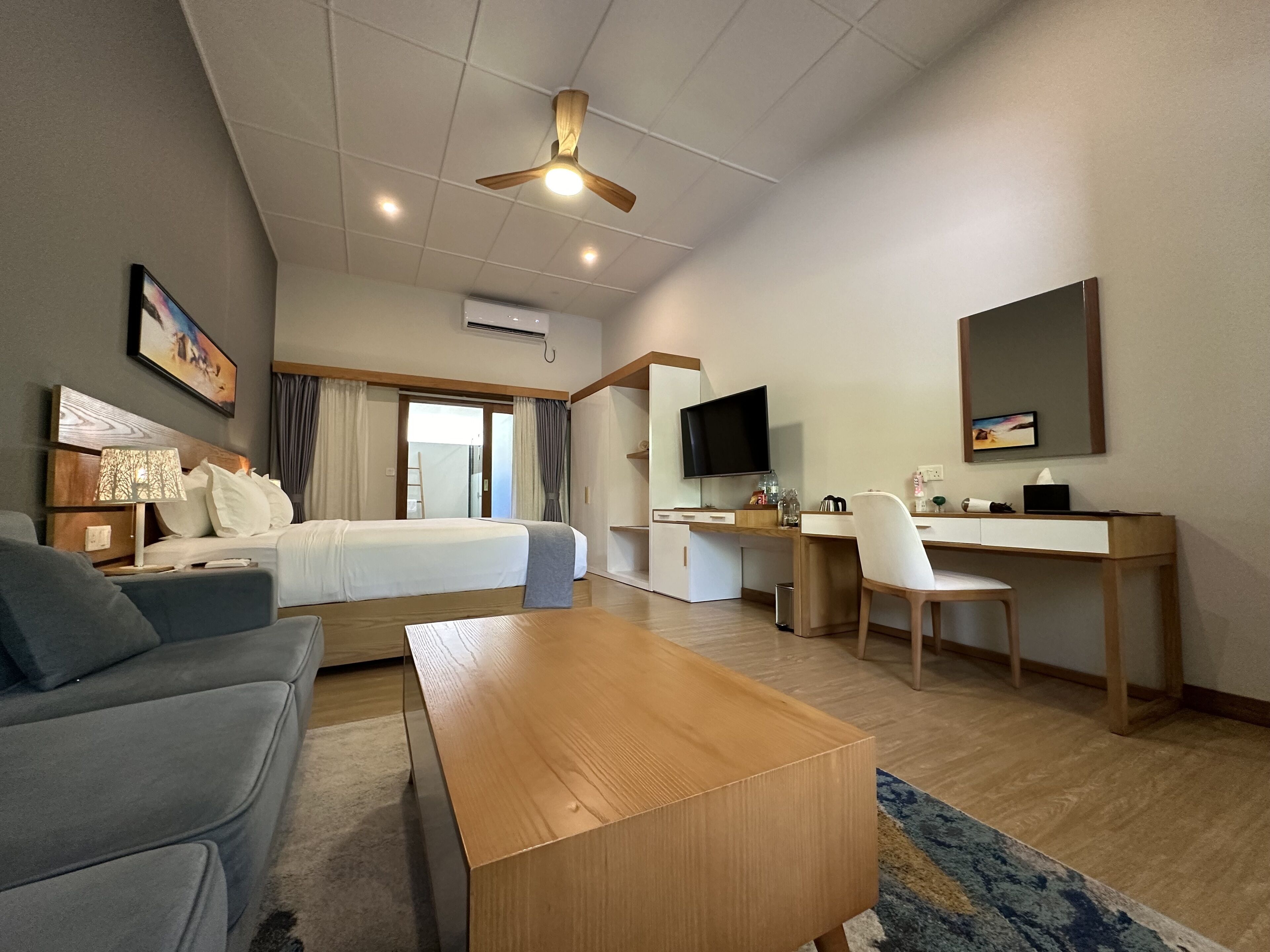 A hotel room with a bed, a desk, a chair, a television, and a ceiling fan.